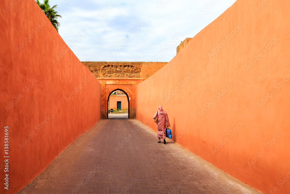 Obraz premium Muslim woman walking through a narrow street with gate in Marrakech