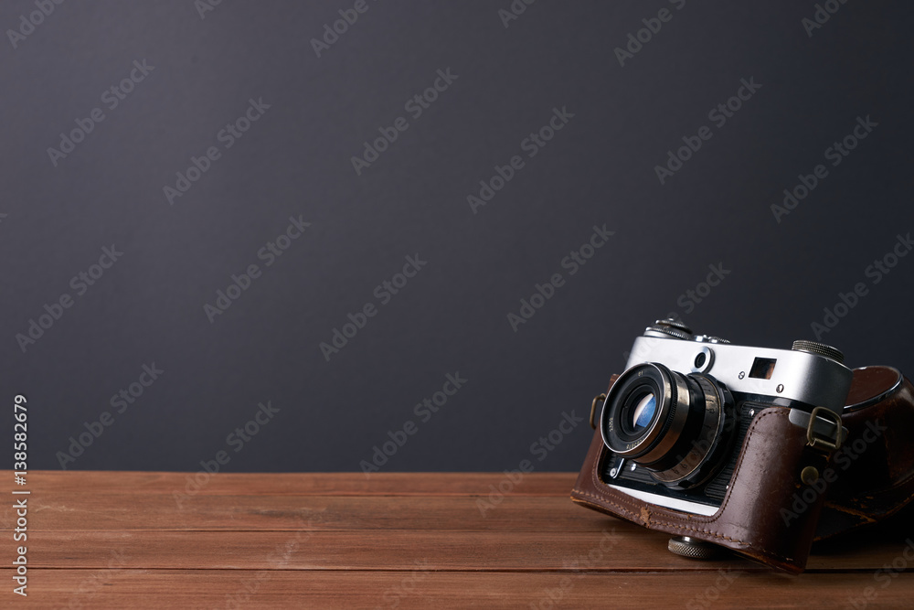 Old retro camera in leather case on vintage wooden boards black