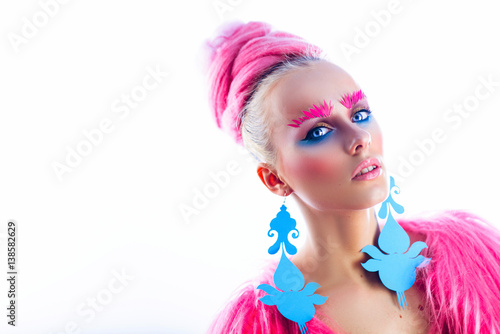 Girl model with blue eyes in a pink coat and blue earrings. Art hairstyle and makeup. On a white background. advertising space