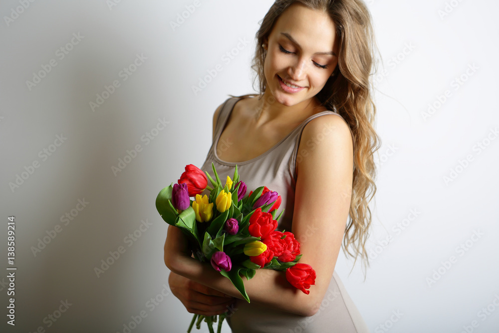 Feminine gentle smiling girl with colorful tulips in hands. Looking at the flowers, springtime Feminine gentle smiling girl with colorful tulips in hands. Looking at the flowers, springtime