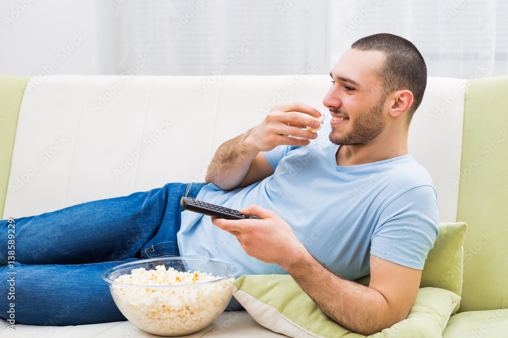 Young man enjoys watching tv and eating popcorn. Young man enjoys watching tv and eating popcorn.