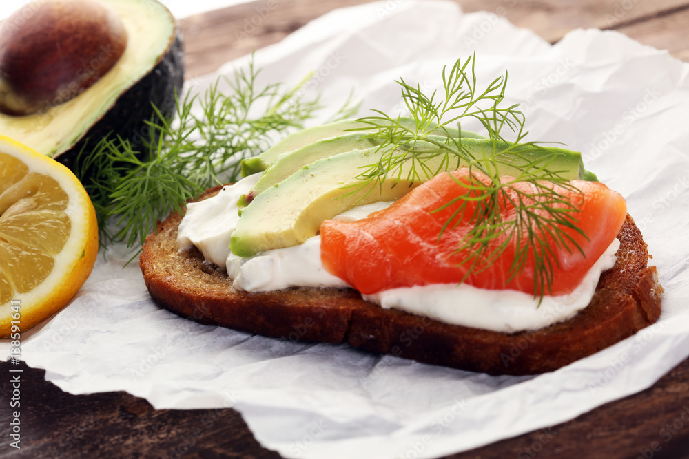 Bread with avocado and smoked salmon for lunch table. Sharing antipasti on party or summer picnic time over wooden rustic background. Bread with avocado and smoked salmon for lunch table. Sharing antipasti on party or summer picnic time over wooden rustic background.