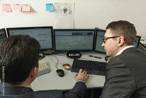 Two men working together for the computers in the office engaged in trading
