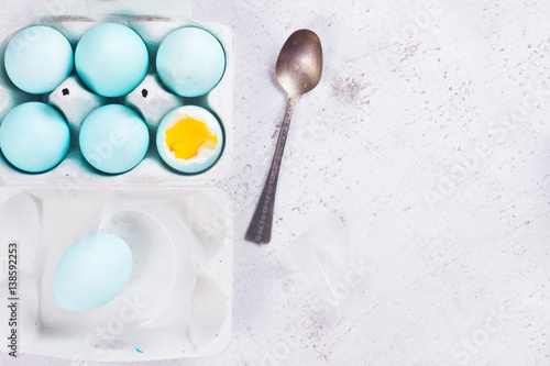 Set of blue easter eggs, one with yolk, spoon, top view on wooden aged table