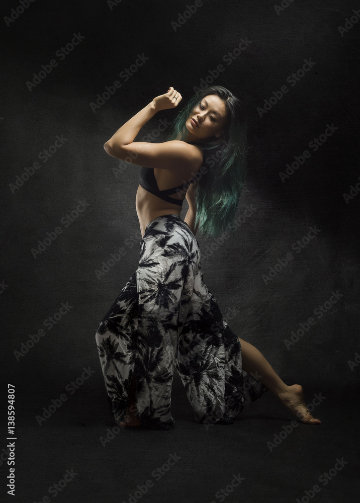 beautiful strong asian with long green hair dances with sensual dramatic graceful poses on dark textured background  