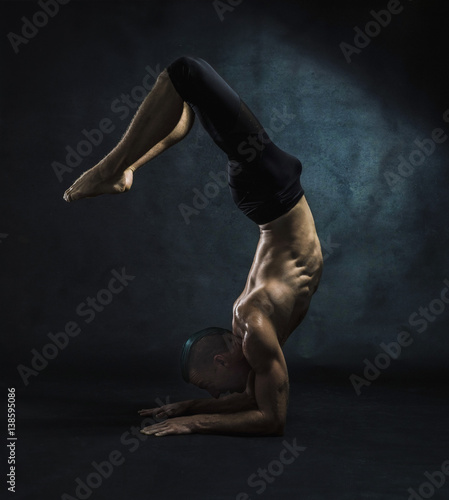 muscular white male with grean streak in his hair performs an elbow stand showing his abs and torso with a textured background 