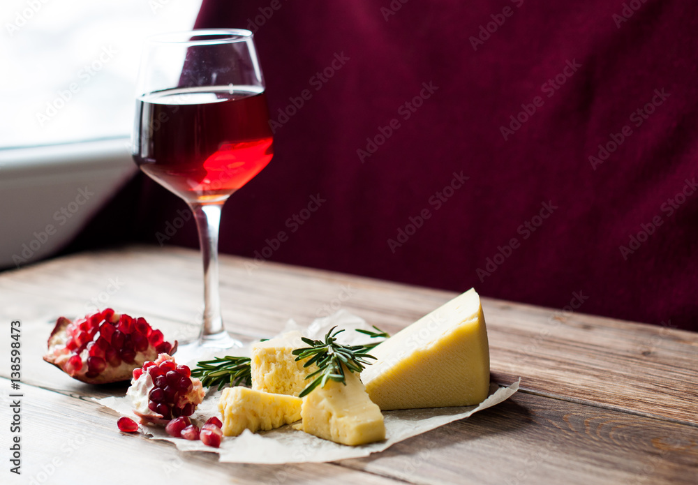 Glass of red wine, pomegranates and cheese on the table. Dark background. agriculture and farming. Banner for restaurant Glass of red wine, pomegranates and cheese on the table. Dark background. agriculture and farming. Banner for restaurant