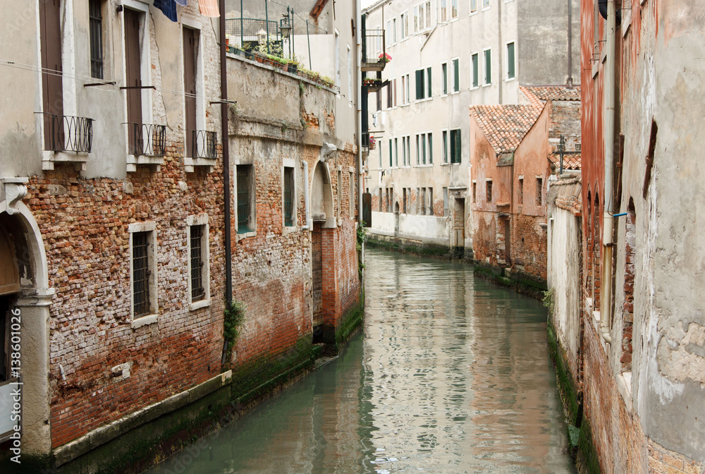 The river flows through the narrow streets of Venice between old houses in Italy