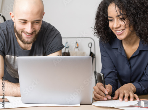 Two young business people smiling. Looking on the laptop monitor.
