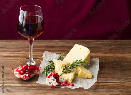 Cup with red wine, cheese and fruit on the table. Pomegranates on a dark background. Banner for restaurant
