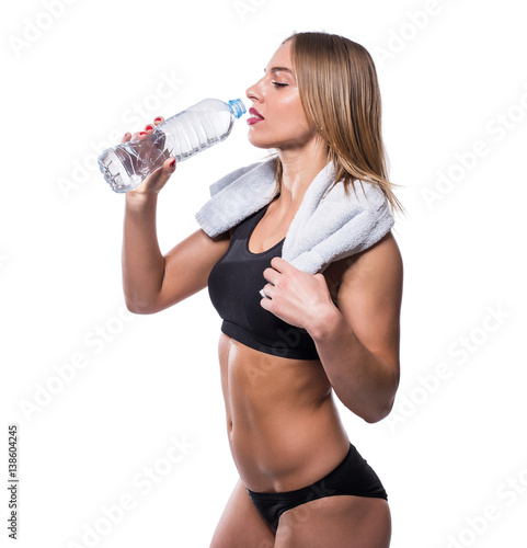 Attractive sexy woman after workout with towel and shaker isolated over white background. Healthy girl drinks pure water.