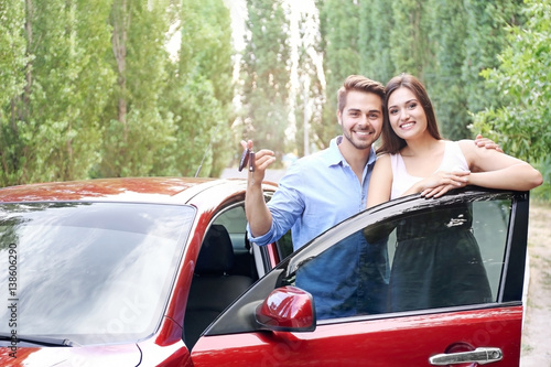 Beautiful young couple standing near red car with keys
