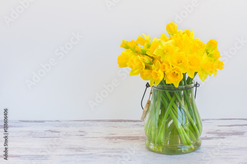Slika na platnu Posy of bright yellow daffodils on white wooden table wih copy space