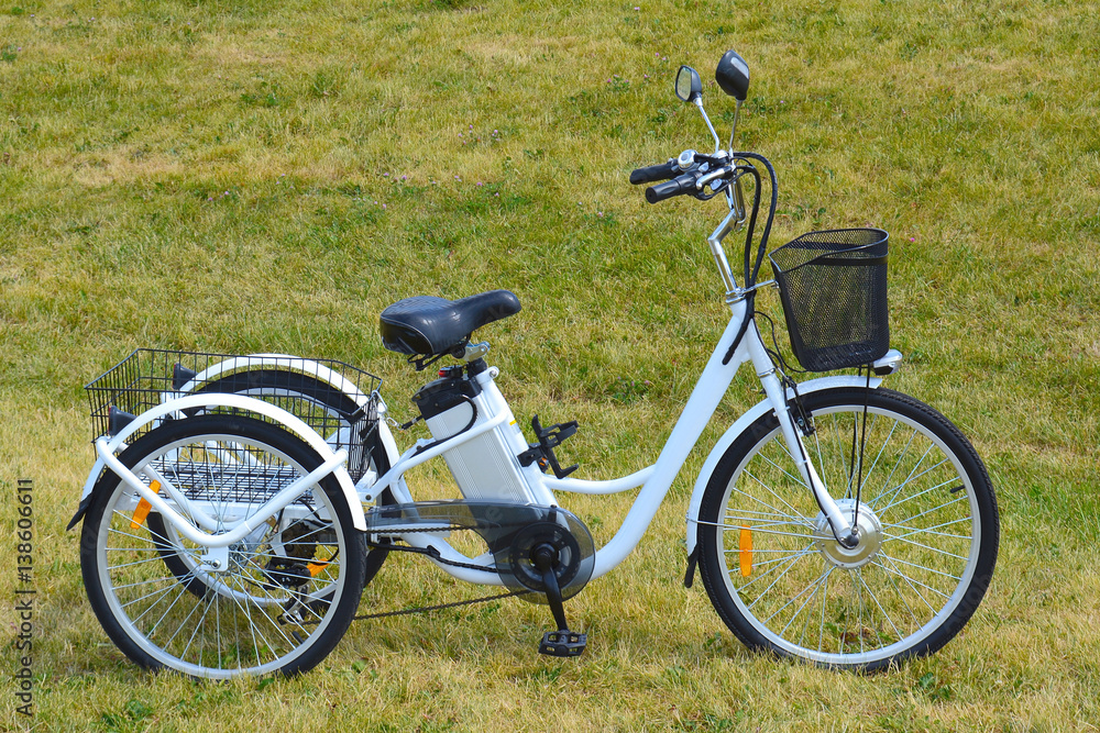 Electric trike or bicycle in the park in sunny summer day. Shot from the side. Unfiltered, with natural lighting. The view of the e motor and power battery of the three wheel bike. Electric trike or bicycle in the park in sunny summer day. Shot from the side. Unfiltered, with natural lighting. The view of the e motor and power battery of the three wheel bike.