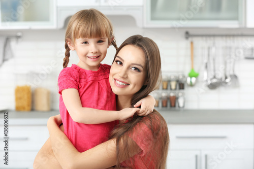 Young mother embracing little girl at kitchen