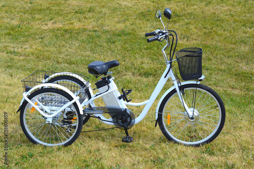 Electric trike or bicycle in the park in sunny summer day. Shot from the side. Unfiltered, with natural lighting. The view of the e motor and power battery of the three wheel bike.