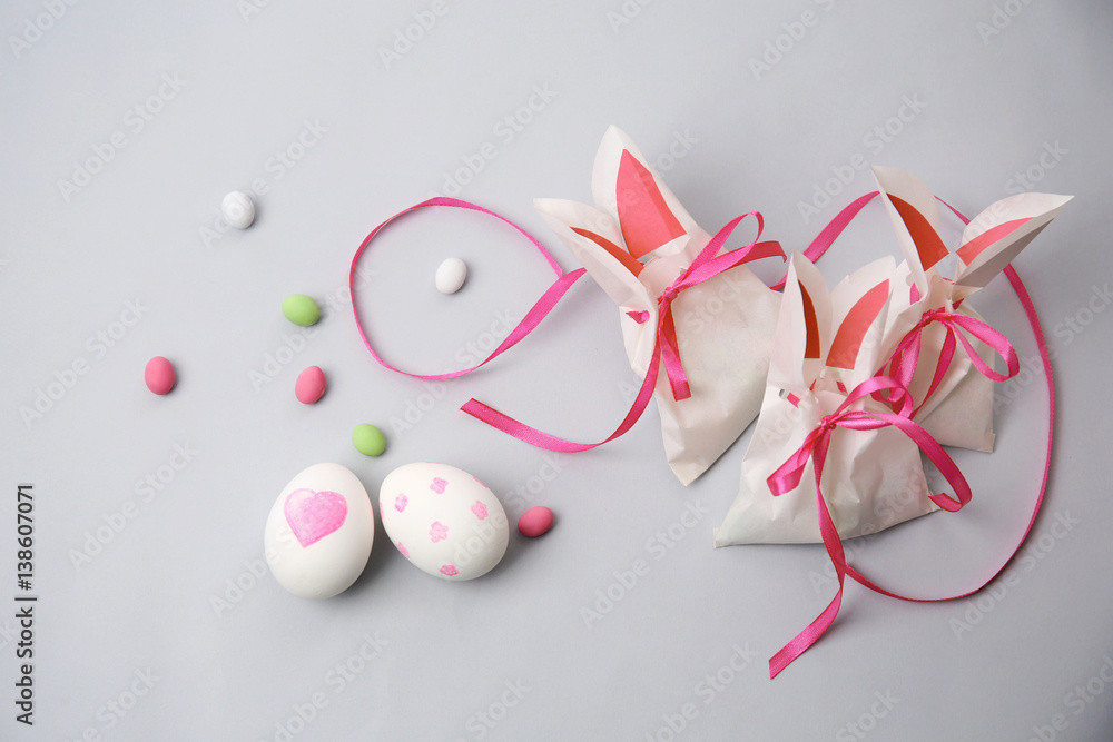 Paper bags in shape of Easter rabbits, painted eggs and candies on light background