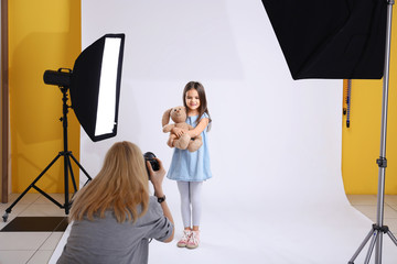 Photographer taking photo of cute little girl with toy bear on light background