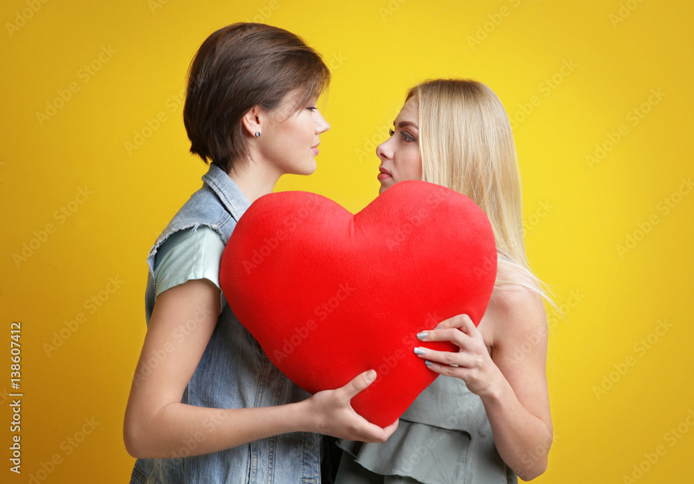 Young lesbian couple with decorative heart on color background