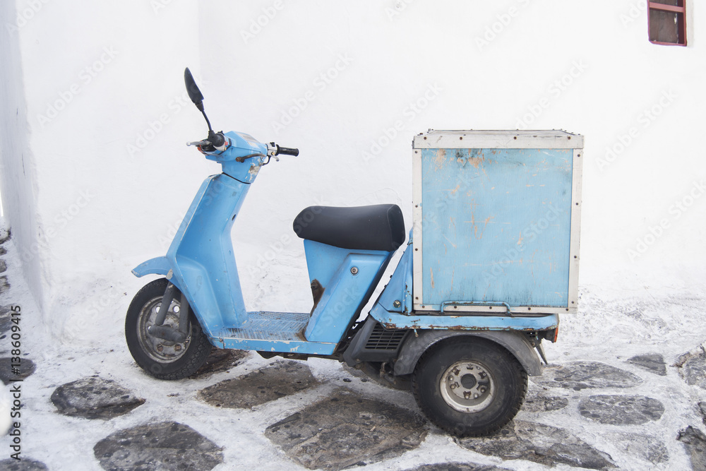 light blue delivery moped scooter parked in front of a whitewashed wall on the streets Mykonos, Greece Stock Photo | Stock