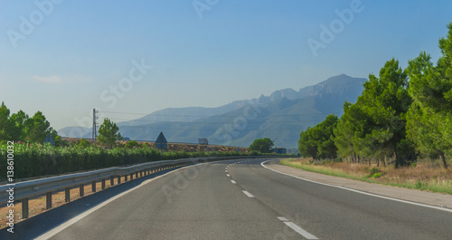 Sunshine on Coastal highway. Lone white car drives along through foothills and mountain ranges on the edges of continental Europe in rural Spain. 