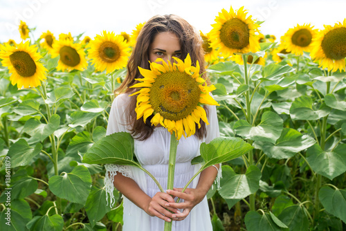 cheerful girl looks out from sunflower in a field