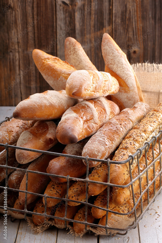 Different types of baguettes in metal basket in bakery on wooden background