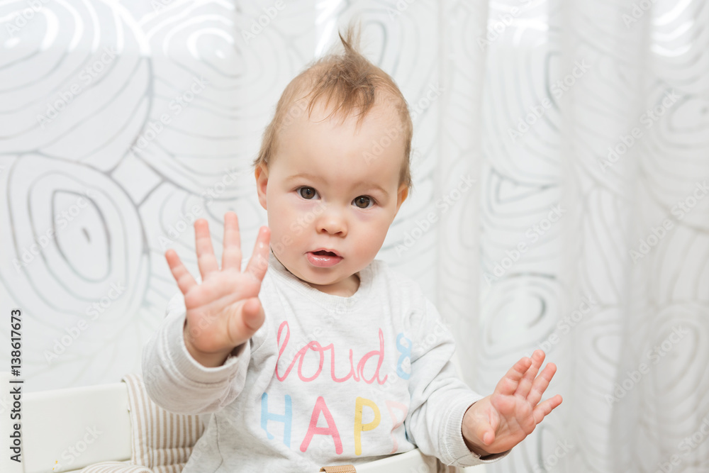 Eleven months old baby girl sitting in a stool making funny faces into the camera, raising her both hands in the air Eleven months old baby girl sitting in a stool making funny faces into the camera, raising her both hands in the air