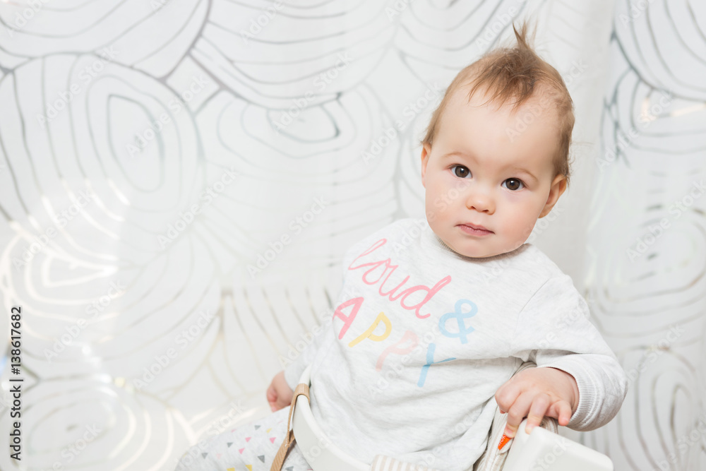 Eleven months old baby girl sitting in a stool making funny faces into the camera Eleven months old baby girl sitting in a stool making funny faces into the camera