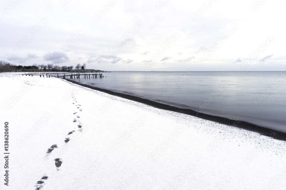 Footprints leading down a snoy beach, restful scene with cloudscape, rustic pier and blue waters