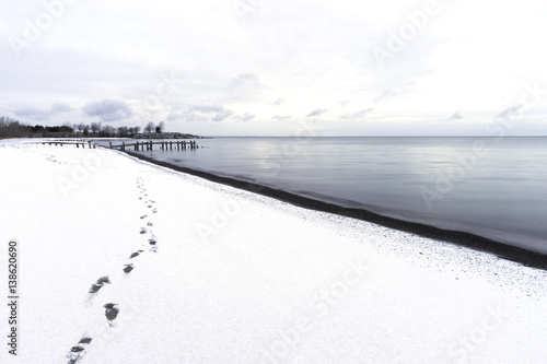 Footprints leading down a snoy beach, restful scene with cloudscape, rustic pier and blue waters photo