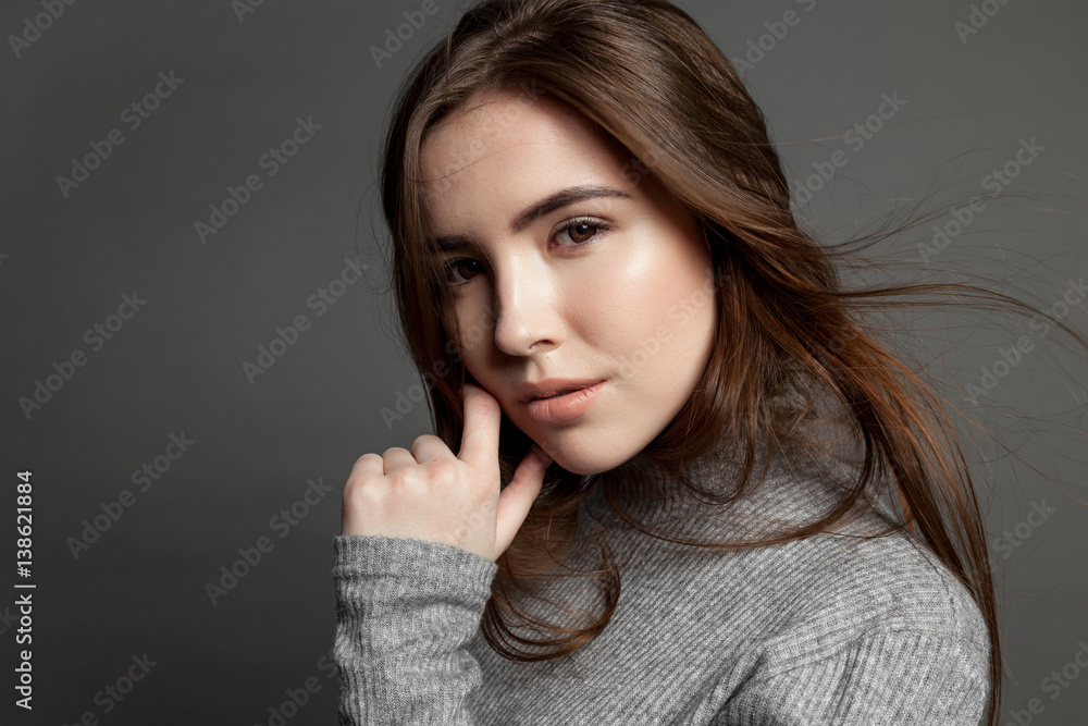 Brunette female cute model girl with flying hair on a gray background looking at the camera Brunette female cute model girl with flying hair on a gray background looking at the camera