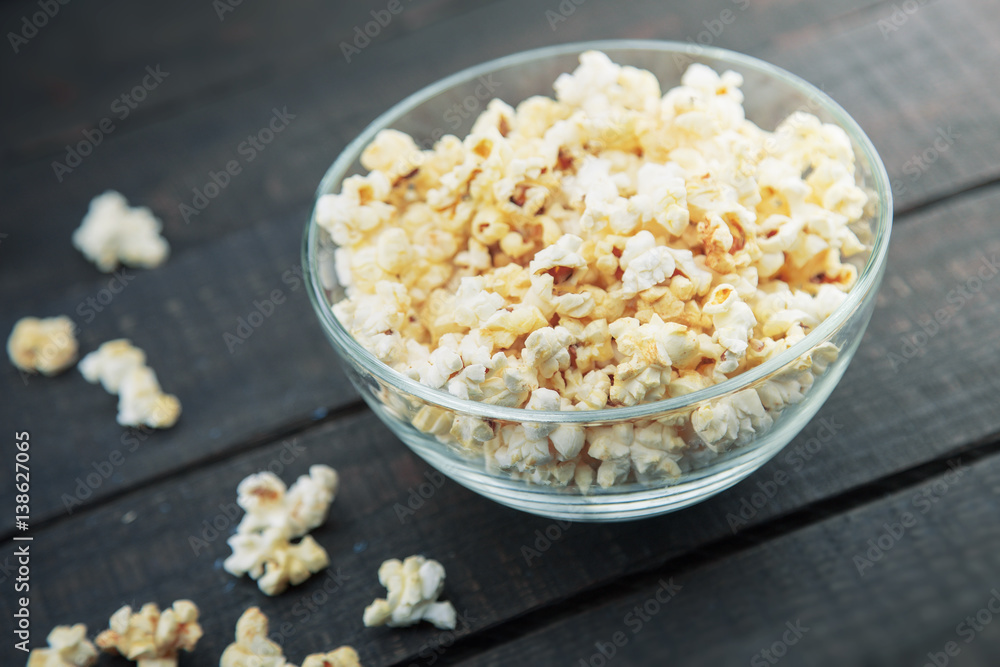 Glass bowl with freshly popped popcorn with salt on dark wooden background. Soft focus. Glass bowl with freshly popped popcorn with salt on dark wooden background. Soft focus.