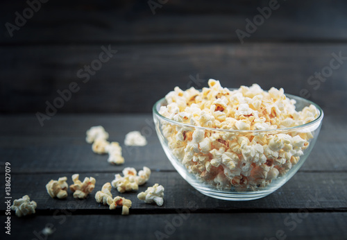 Glass bowl with freshly popped popcorn with salt on dark wooden background. Soft focus.