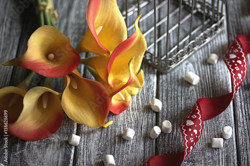 orange yellow calla lilies with red ribbon and white marshmallows on wooden gray background
