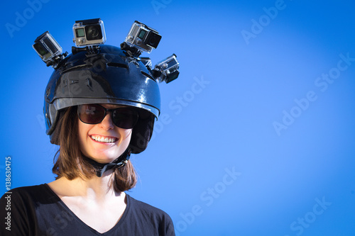 Une jeune femme souriante porte un casque avec quatre caméras de sport fixées dessus