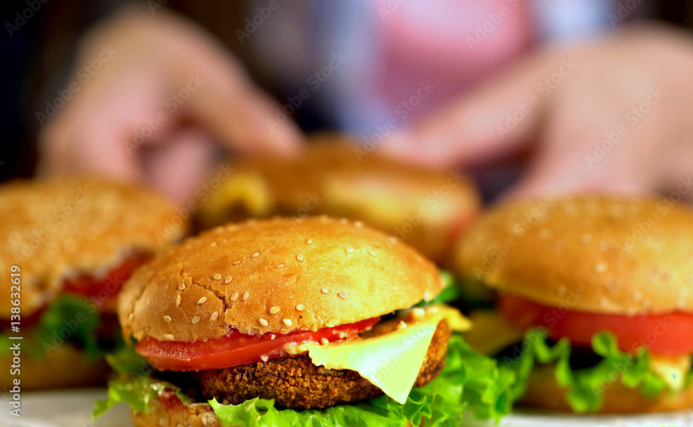 Mini hamburger buns. Fast food with ham on wooden board . Group of hamburger. Human hand holding cheeseburger. Sharpness in front of sandwich. Mini hamburger buns. Fast food with ham on wooden board . Group of hamburger. Human hand holding cheeseburger. Sharpness in front of sandwich.