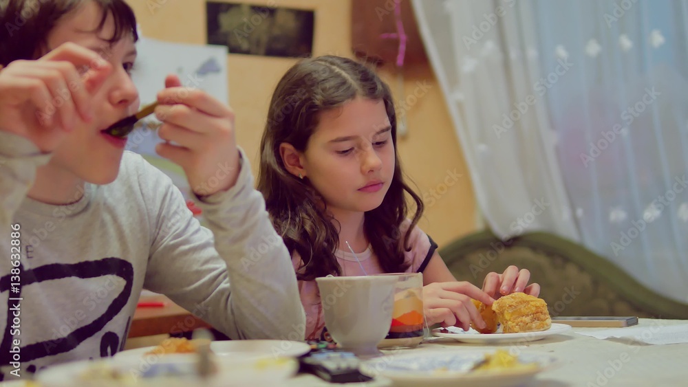 boy and girl family children are eating at table, drink tea and eat cake, watching tv boy and girl family children are eating at table, drink tea and eat cake, watching tv