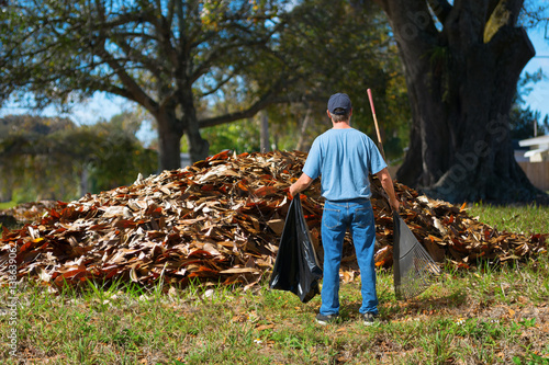 Cuadro en lienzo A distraught man with a rake and garbage bag in his hands is standing in front o