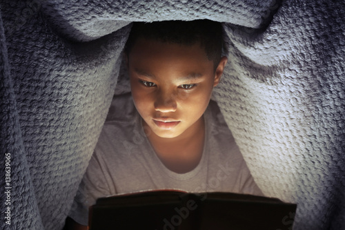 Cute boy reading book at night