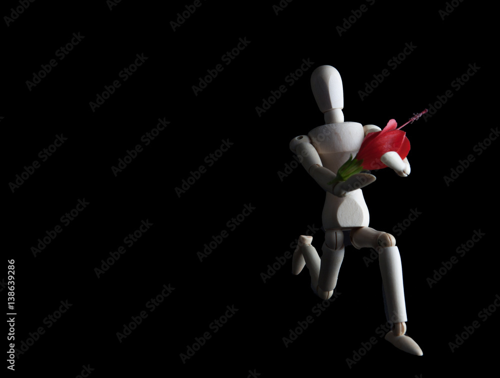 Wooden figurine kneeling with flower on black background with copy space. High contrast lighting. Wedding, engagement, valentines concept Wooden figurine kneeling with flower on black background with copy space. High contrast lighting. Wedding, engagement, valentines concept