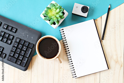 Business concept : Flat lay style of office workspace desk with blank notebook paper, computer keyboard, cup of coffee and action camera, top view mock up