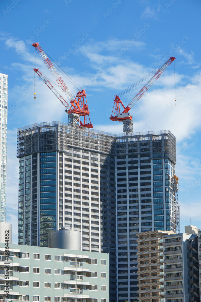 Many tall buildings under construction and cranes under a blue sky near Sumida River at Tokyo, Japan