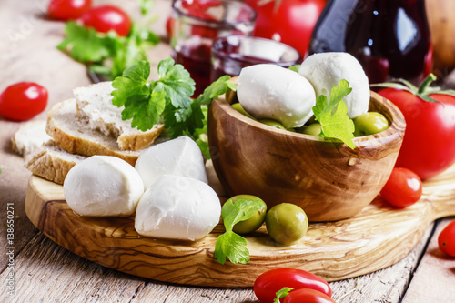 Mozzarella cheese with green olives and tomatoes, old wooden background, selective focus