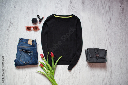 Fashion concept. Black sweater, tulips, blue jeans, black bag, sunglasses, lipstick. Spring wardrobe. Wooden background. top view photo