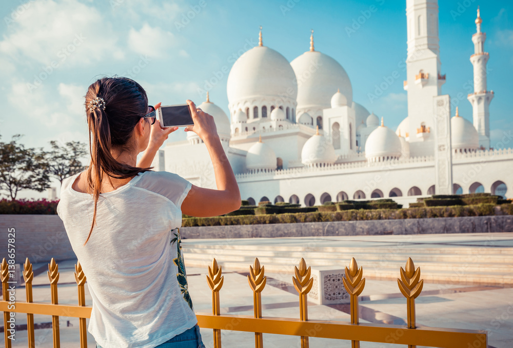 Fototapeta premium Młoda turystka strzelająca z telefonu komórkowego Sheikh Zayed wielki biały meczet w Abu Zabi, Zjednoczone Emiraty Arabskie, Zatoka Perska. Zjednoczone Emiraty Arabskie są znanym miejscem turystycznym