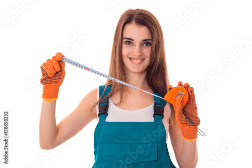 Happy young brunette woman builder in uniform with gloves makes renovation and looking at the camera and smiling isolated on white background