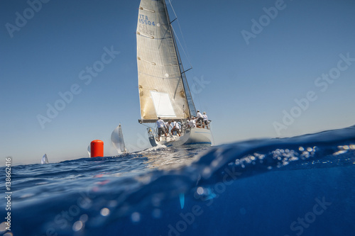 Sailing boat with yellow spinnaker and red buoy. Calm sea.