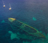Bird view on the ship wreck in croatian sea with snorkeling people and two boats anchoring in background.