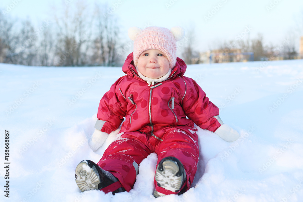 baby girl 11 months in warm clothes sits on snow outdoor in winter